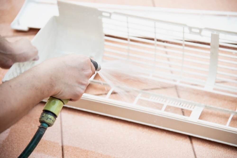 Technician pressure washing the filter panels of an air conditioner indoor unit